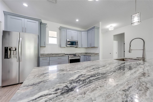 kitchen with a sink, stainless steel appliances, light stone counters, and gray cabinets