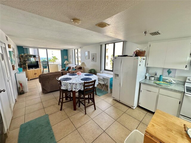 kitchen with a textured ceiling, white fridge with ice dispenser, light tile patterned floors, and white cabinets