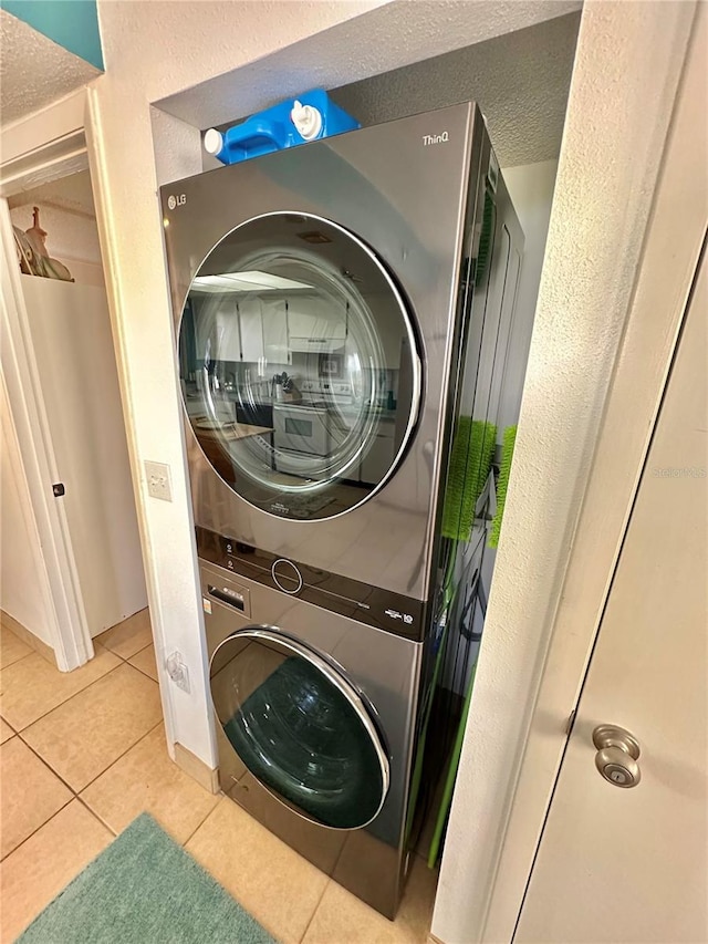 laundry room with a textured ceiling, stacked washer / drying machine, and light tile patterned flooring