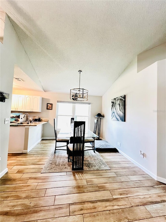 dining space featuring a textured ceiling, light wood-type flooring, a chandelier, and lofted ceiling