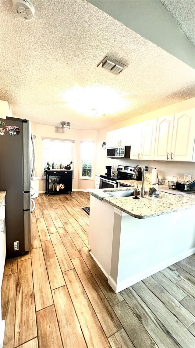 kitchen featuring white cabinets, kitchen peninsula, light hardwood / wood-style flooring, stainless steel appliances, and light stone countertops