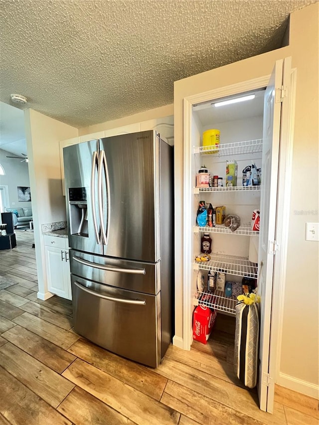 kitchen with a textured ceiling, light hardwood / wood-style floors, white cabinetry, and stainless steel fridge with ice dispenser