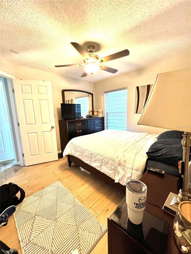 bedroom with light wood-type flooring, ceiling fan, and a textured ceiling