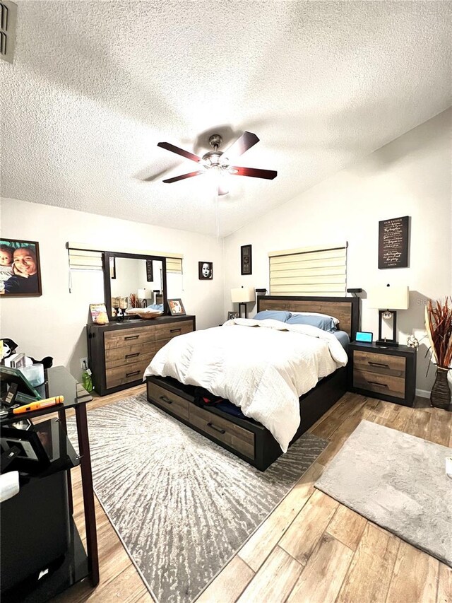 bedroom with light hardwood / wood-style flooring, vaulted ceiling, ceiling fan, and a textured ceiling