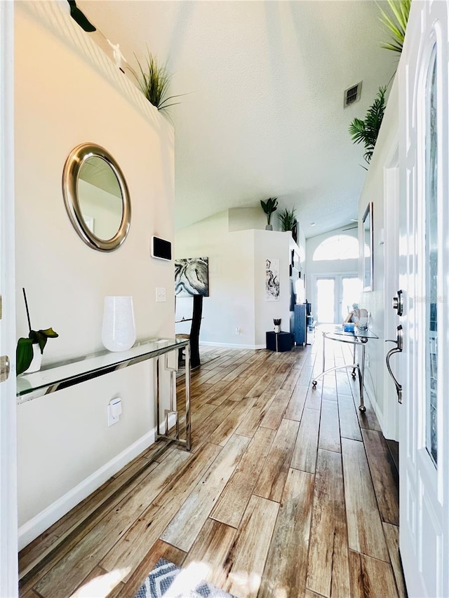 hall featuring visible vents, baseboards, vaulted ceiling, and wood finished floors