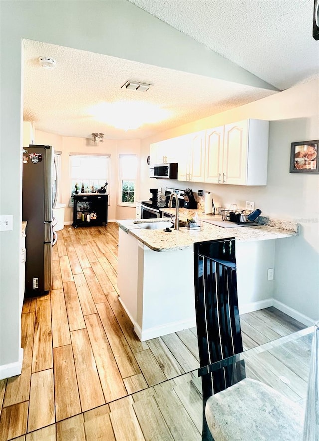 kitchen with a textured ceiling, appliances with stainless steel finishes, white cabinets, and light wood-style floors