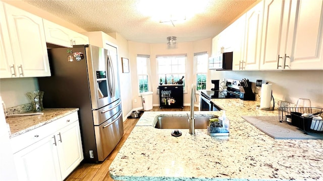kitchen with a textured ceiling, light wood-type flooring, appliances with stainless steel finishes, light stone counters, and a sink