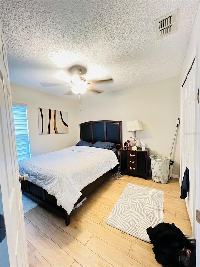 bedroom with a closet, a textured ceiling, a ceiling fan, visible vents, and light wood finished floors