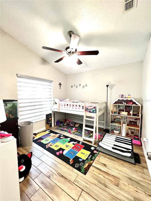 bedroom with visible vents, a ceiling fan, a textured ceiling, wood finished floors, and lofted ceiling