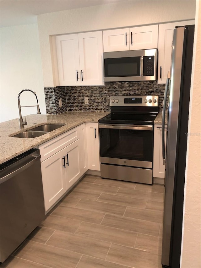 kitchen with sink, white cabinetry, stainless steel appliances, light stone countertops, and decorative backsplash