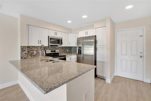 kitchen with light stone counters, appliances with stainless steel finishes, kitchen peninsula, and white cabinets