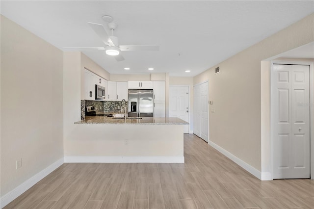 kitchen with white cabinetry, stainless steel appliances, light stone counters, tasteful backsplash, and kitchen peninsula