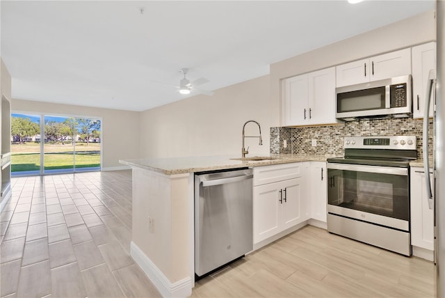 kitchen with sink, appliances with stainless steel finishes, backsplash, white cabinets, and kitchen peninsula