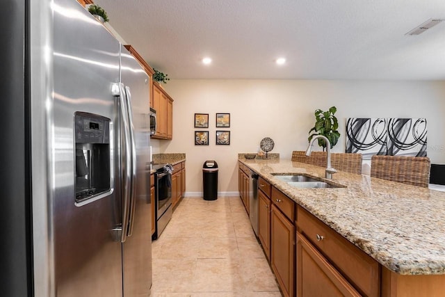 kitchen with appliances with stainless steel finishes, light stone counters, light tile patterned floors, a textured ceiling, and sink