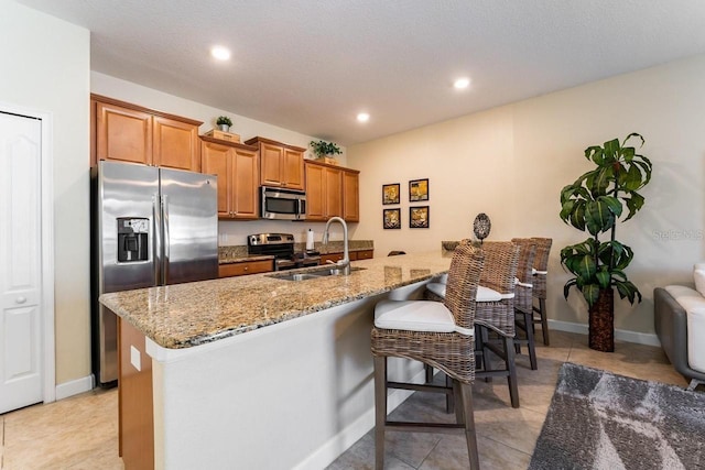 kitchen with appliances with stainless steel finishes, light stone countertops, a breakfast bar area, and sink