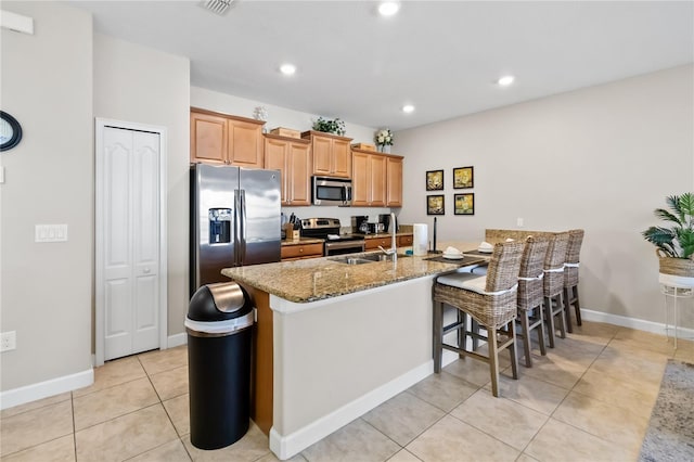 kitchen featuring light tile patterned floors, appliances with stainless steel finishes, a breakfast bar area, light stone countertops, and recessed lighting