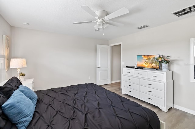 bedroom with light wood-style floors, ceiling fan, visible vents, and baseboards