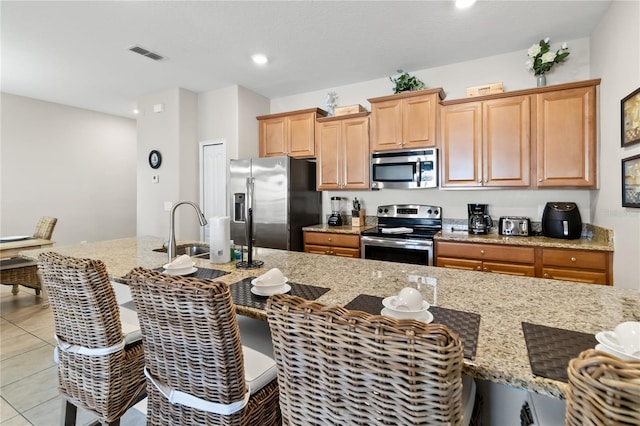 kitchen with light tile patterned flooring, a breakfast bar, visible vents, appliances with stainless steel finishes, and light stone countertops