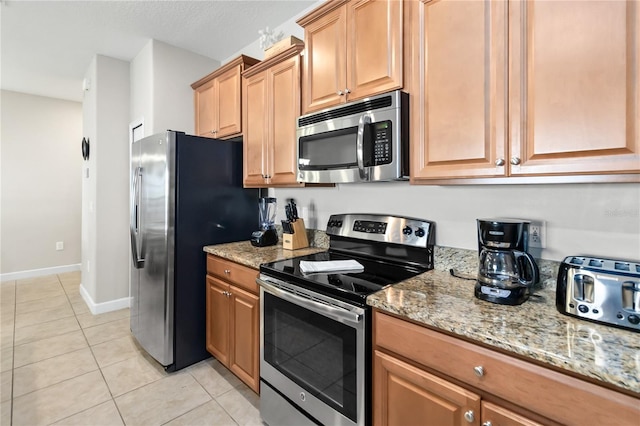 kitchen featuring appliances with stainless steel finishes, baseboards, light stone counters, and light tile patterned floors