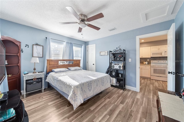 bedroom featuring connected bathroom, light hardwood / wood-style floors, ceiling fan, and a textured ceiling