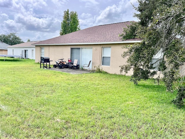 324 Baccarat Ct, Kissimmee, FL 34759 - back of house with roof with shingles, a trampoline, a yard, a patio, and stucco siding