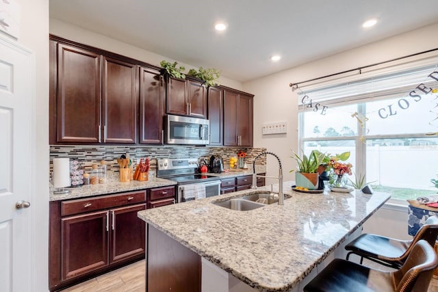 kitchen with stainless steel appliances, sink, light stone counters, light hardwood / wood-style flooring, and decorative backsplash