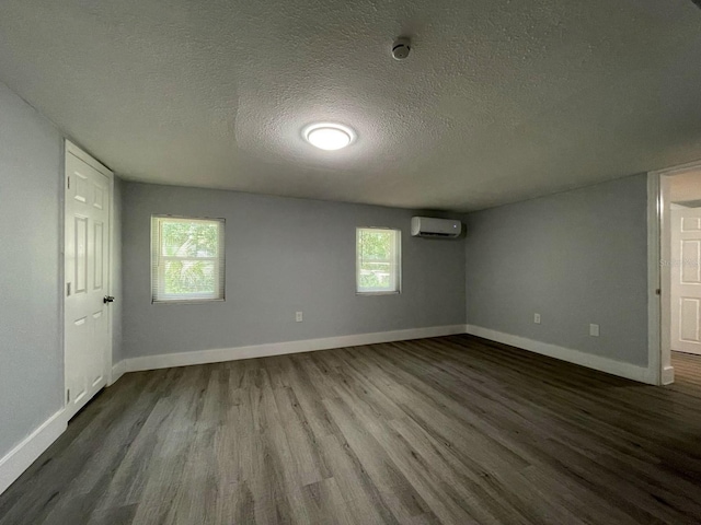 empty room with a textured ceiling, wood-type flooring, an AC wall unit, and a wealth of natural light