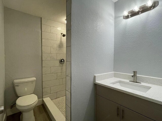 bathroom with vanity, toilet, a textured ceiling, and tiled shower