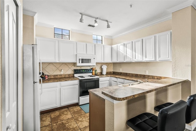 kitchen with kitchen peninsula, decorative backsplash, white appliances, and white cabinetry