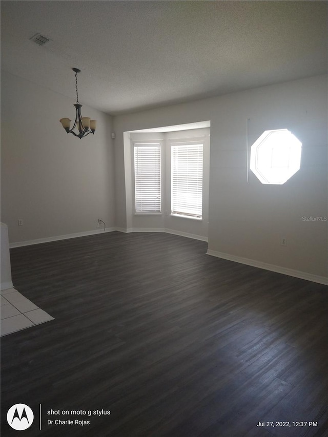 spare room featuring a notable chandelier, dark hardwood / wood-style flooring, and a textured ceiling