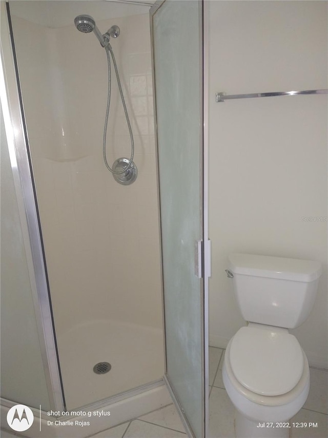 bathroom featuring a shower with door, tile patterned floors, and toilet