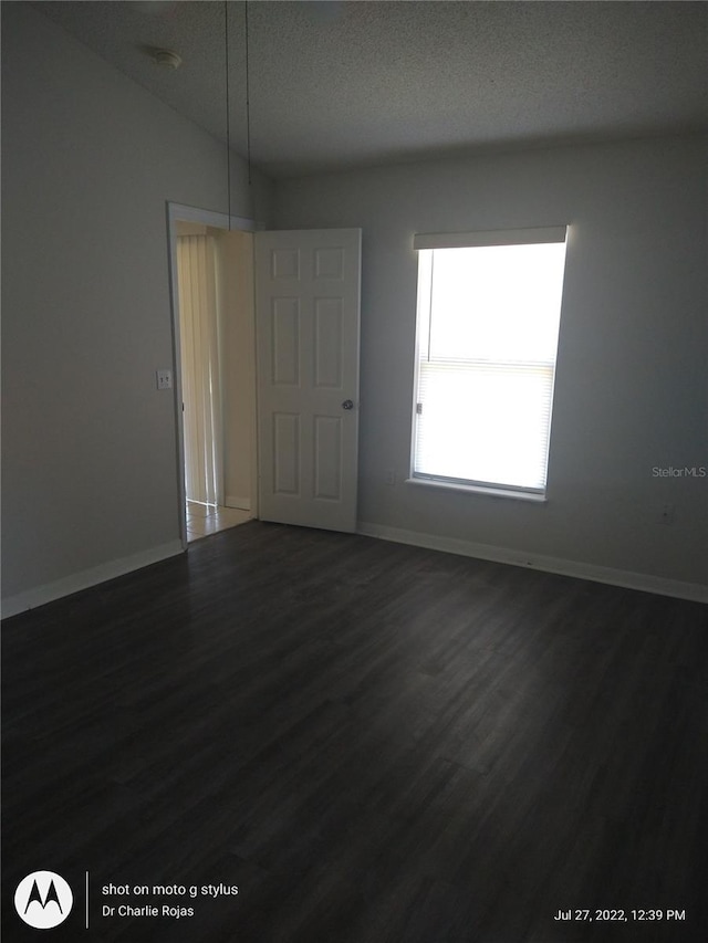 spare room featuring vaulted ceiling, a textured ceiling, and dark hardwood / wood-style flooring