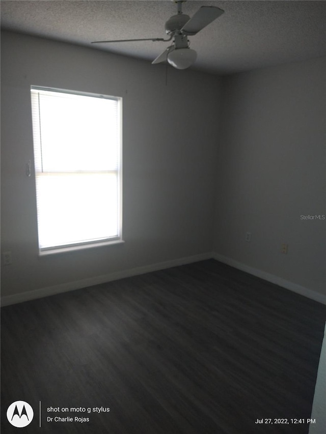 empty room with ceiling fan, dark wood-type flooring, and a textured ceiling