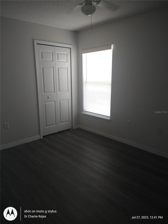 unfurnished bedroom with ceiling fan, a closet, dark wood-type flooring, and a textured ceiling