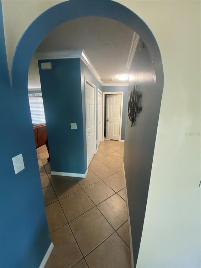 hall featuring arched walkways, tile patterned flooring, baseboards, and ornamental molding