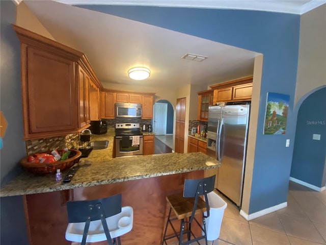 kitchen featuring arched walkways, appliances with stainless steel finishes, decorative backsplash, and a sink