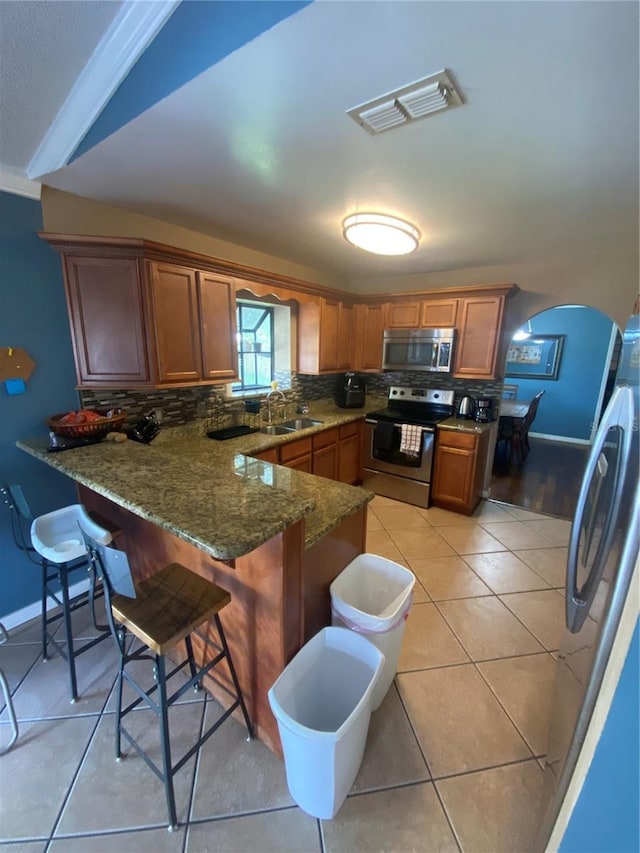 kitchen featuring stainless steel appliances, a peninsula, a sink, tasteful backsplash, and visible vents