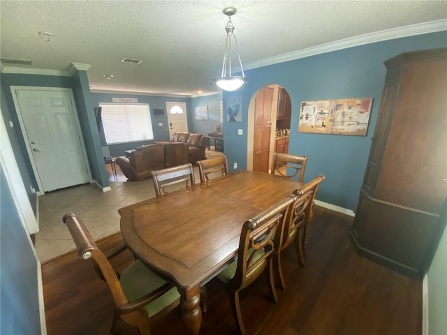 dining room with arched walkways, crown molding, wood finished floors, and a textured ceiling