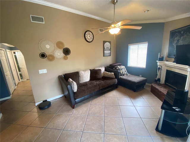 tiled living room with arched walkways, visible vents, a ceiling fan, and ornamental molding