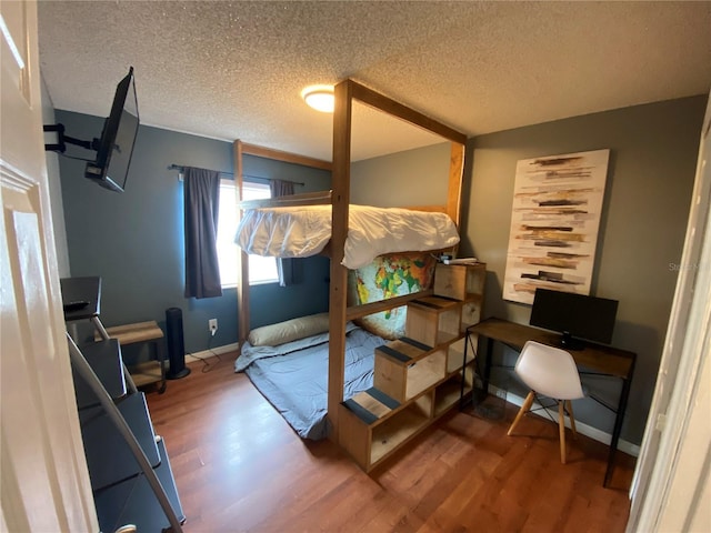 bedroom with wood finished floors, a textured ceiling, and baseboards