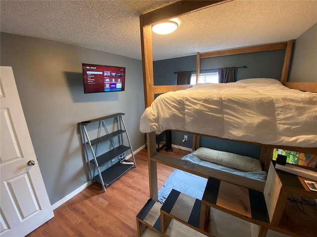 bedroom with baseboards, wood finished floors, and a textured ceiling