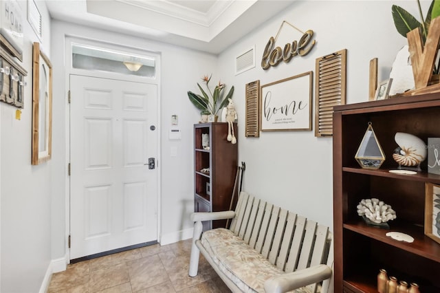 foyer entrance with light tile patterned flooring, ornamental molding, and a tray ceiling