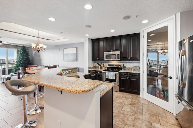 kitchen with a textured ceiling, decorative light fixtures, stainless steel appliances, a kitchen breakfast bar, and a notable chandelier