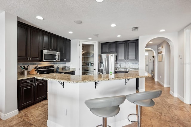 kitchen with a kitchen breakfast bar, a textured ceiling, a kitchen island, and stainless steel appliances