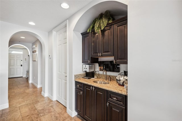 kitchen with dark brown cabinets, light stone counters, and sink