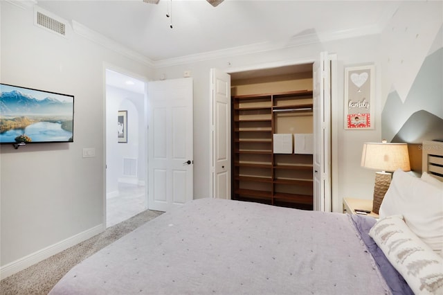 carpeted bedroom featuring ceiling fan, a closet, crown molding, and a spacious closet