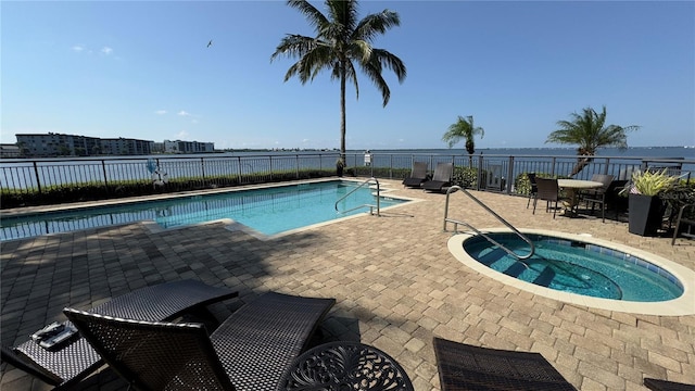 view of swimming pool featuring a hot tub, a water view, and a patio area