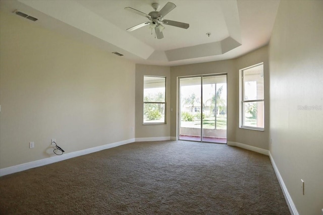 empty room featuring dark carpet, ceiling fan, and a raised ceiling