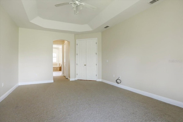 unfurnished bedroom featuring ceiling fan, a raised ceiling, and light carpet