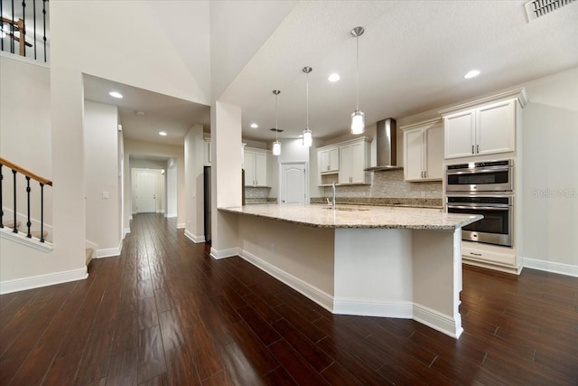 kitchen featuring white cabinets, decorative light fixtures, wall chimney range hood, and decorative backsplash